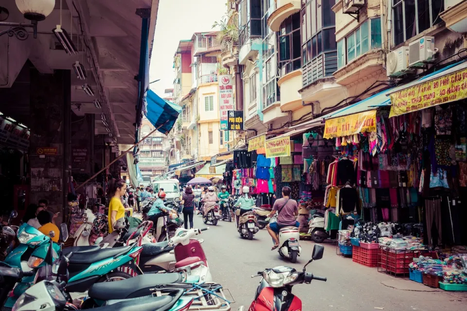 People on motorbikes driving through busy vibrant Hanoi, Vietnam produce market.